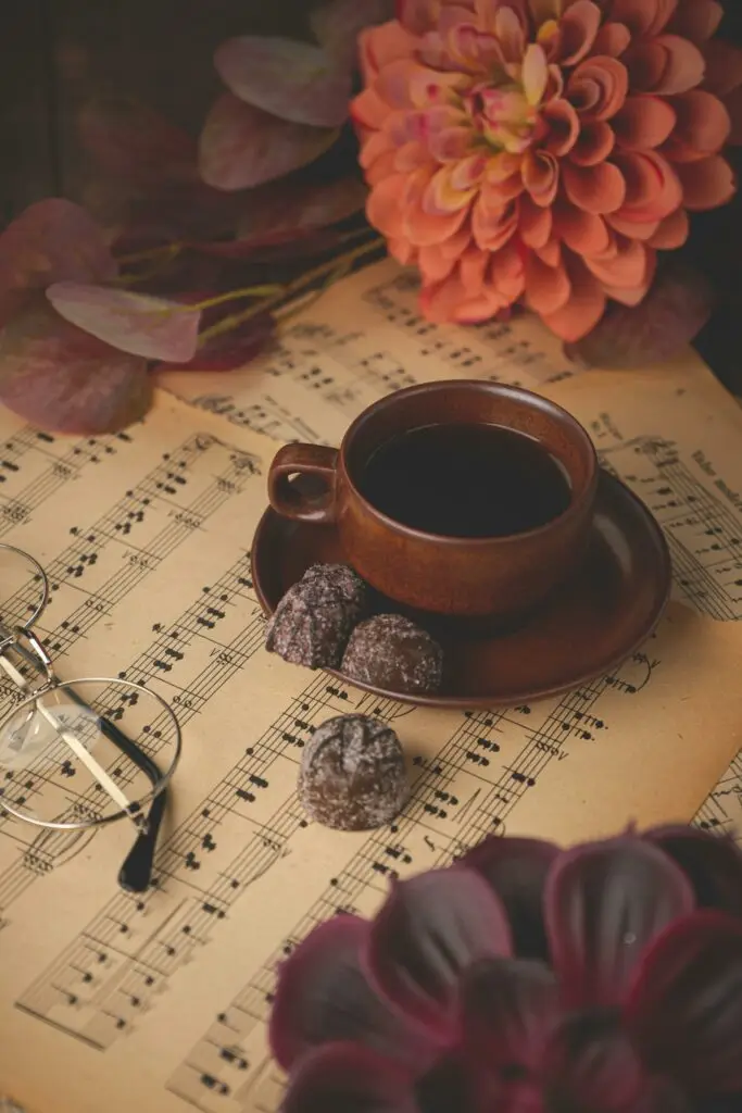 Warm autumn coffee setup with chocolates on vintage sheet music, surrounded by flowers.